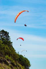 three parachutes simultaneously descend near a cliff against a blue sky