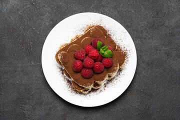 portion of Classic tiramisu dessert with raspberries on dark concrete background