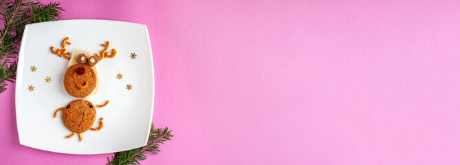 Funny Christmas new year's deer of food: cookies, bread, pretzels, candy on a white square plate with snowflakes on a pink background and space for text. Banner for new year and Christmas.