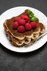 portion of Classic tiramisu dessert with raspberries on dark concrete background