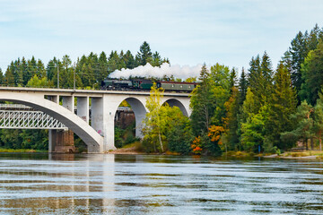 Kouvola, Finland - 18 September 2020: Autumn landscape of bridge with moving old steam passenger train Ukko-Pekka and Kymijoki river waters in Finland, Kouvola, Koria