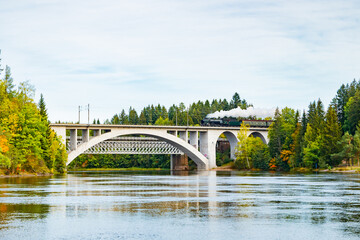 Kouvola, Finland - 18 September 2020: Autumn landscape of bridge with moving old steam passenger train Ukko-Pekka and Kymijoki river waters in Finland, Kouvola, Koria