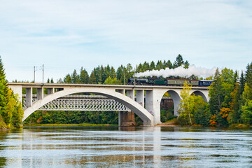 Kouvola, Finland - 18 September 2020: Autumn landscape of bridge with moving old steam passenger train Ukko-Pekka and Kymijoki river waters in Finland, Kouvola, Koria