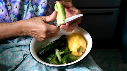 Wrinkled mature hands cut cucumber into bowl of fresh vegetables
