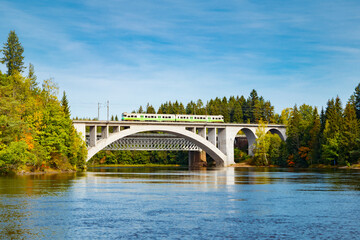 Obraz premium Autumn landscape of bridge with moving passenger train and Kymijoki river waters in Finland, Kouvola, Koria