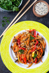 Korean eggplants. Spicy vegetable salad with eggplant, bell peppers, carrots, onions on a plate on a black background.