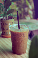 Vintage style photo Black iced coffee in a clear plastic mug sits on a wooden table in a small cafe.