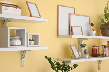 Shelves with products, decor and blank frames in kitchen