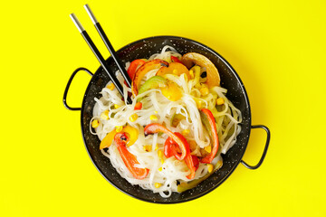 Frying pan with tasty rice noodles and vegetables on color background