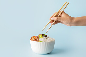 Woman eating tasty rice noodles on color background