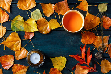 Fototapeta na wymiar Autumn background with a cup of tea and a candle with autumn leaves, shot from the top with a place for text, on a dark blue wooden background