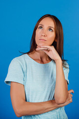 Portrait of a brooding brunette in a blue t-shirt, looking into an empty space, isolated on a blue background.