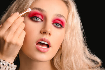 Young woman applying beautiful eyeshadows against dark background