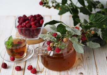Autumn late raspberries. Useful properties of medicinal tea with raspberries.Branch with raspberries on a glass teapot with tea on a light background.