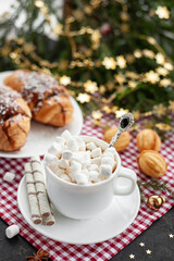 Christmas breakfast. Christmas morning. A cup of cocoa with marshmallows and croissants on a light concrete background with a branch of decorated Christmas tree. Place for text. View from above.