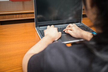 Rear view of young woman working on her laptop computer at home. Happy girl learning technology using keyboard on notebook hardware equipment. Teen student studying online or education internet.