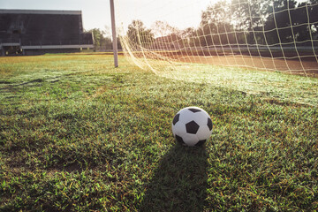 View of classic leather soccer ball on goal net in green grass field the arena stadium. Traditional black and white football equipment to play competitive game. Sports tournament concept. 