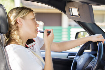 womanmaking up her lips with red lipstick in car