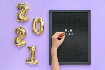 Balloons in shape of figure 2021, hand and board with text NEW YEAR on color background