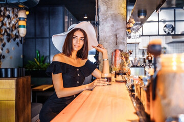 Fototapeta na wymiar An attractive client sitting at the bar with a glass of coffee brewed using an alternative method. A true connoisseur of pure coffee without milk and sugar. Graceful woman in a hat is in a cafe