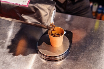 The process of pouring out whole coffee beans from a black pack. Professional barista preparing coffee in the restaurant. Grinding coffee just before brewing for maximum results