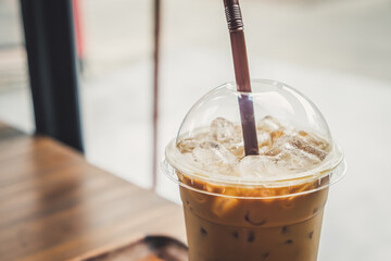 Iced coffee in a plastic cup on a wooden table at the cafe. Cold espresso in the coffee shop with...