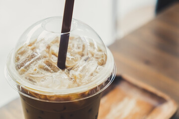 Iced coffee in a plastic cup on a wooden table at the cafe. Cold espresso in the coffee shop with copy space. Beverage glass frozen in the restaurant. Food sales busy interior decoration vintage.