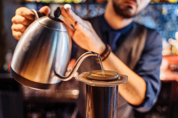Close-up of professional barista hands pouring hot water from a metal kettle into ground coffee beans. An alternative way to make coffee. Coffee filter