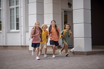 Schoolchildren running happily while leaving school after lessons
