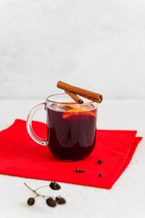 Obraz na płótnie Canvas Homemade mulled wine with cinnamon, anise, cloves and orange in a cup on a red napkin.