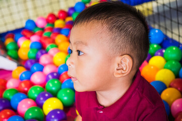 Cute little Asian baby boy relaxing and playing colorful plastic balls at indoor playground center.