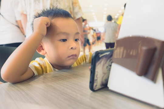 Shot of little Asian baby boy watching something on mobile phone while sitting at home. Cute kid learning technology on the smartphone. Child studying online or education internet.