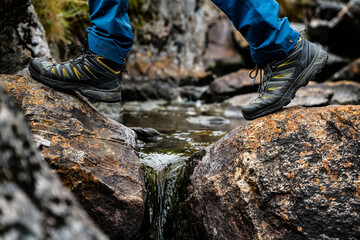 Boots on a hiker, walking on large rocks while crossing a stream in the wild. Close up.