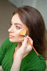 Make up artist applying professional make up of tonal foundation on the face of beautiful young...
