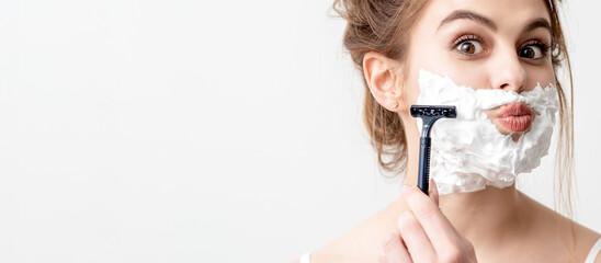 Beautiful young caucasian woman shaving her face by razor on white background. Pretty woman with...