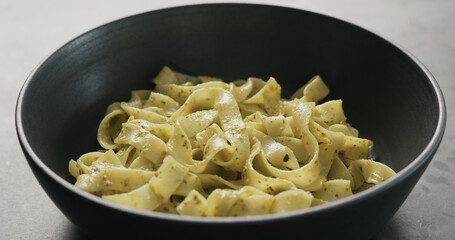 pesto fettuccine in black bowl on concrete countertop