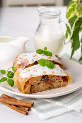 Apple strudel with raisins,  peanuts and cinnamon. A jug of milk.  Light background.