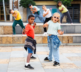 International group of modern tweenagers performing street dance choreography outdoors in summer.