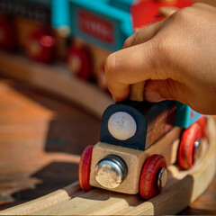 close-up of child's hand playing in the sun with a wooden toy train