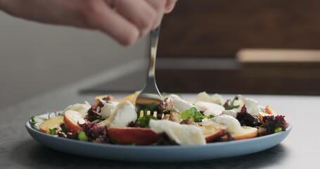 man eat salad with nectarines and mozzarella on a blue plate on concrete countertop on kitchen