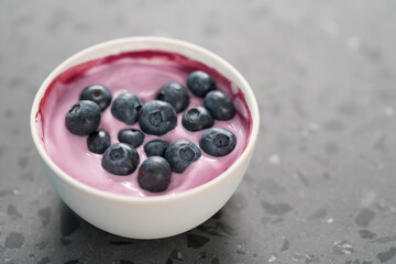 Blueberry yogurt with whole berries in white bowl on concrete background