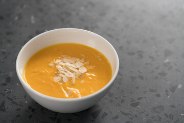 Pumpkin soup puree decorated with almond flakes in white bowl on concrete background