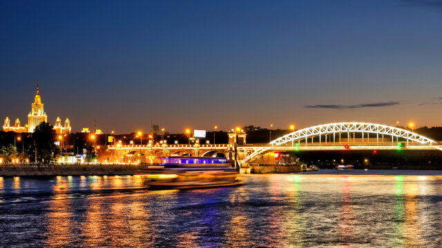 downtown moscow city skyline at night. Historic architecture landmark with Moscow university building and railway bridge reflection on moscow river water against dusk sky background. Wide panorama