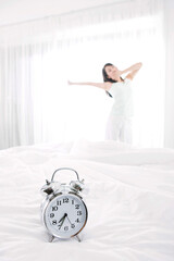 Obraz na płótnie Canvas woman stretching beside the bed and alarm clock