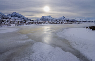 Winter landscape with frozen lake and snow covered mountains in north Norway