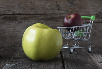 Big green apple and mini supermarkrt cart with red apple on the wooden background.Concept of choice.