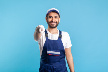 Hey you! Portrait of happy handyman in overalls and gloves, pointing finger to camera. Profession of service industry, builder and house maintenance. Expert repairman in workwear making choice