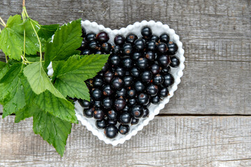 Black currant berries in a white plate in the form of a heart on a wooden background.