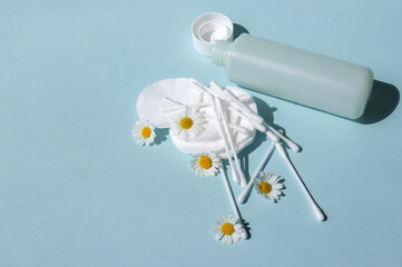 Ear sticks, white cotton pads and chamomiles on a blue background with copy space.