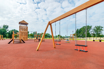 The wooden swing on a new children outdoor playground with red poured in place rubber surface